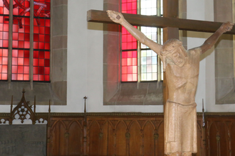 Kruzifix im Chor der Gaildorfer Stadtkirche, im Hintergrund rote Glasfenster | © Petra Natzkowski