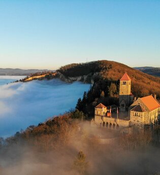 Die Wachenburg thront auf einem Berggrat im Sonnenschein, darunter ist nur Nebel zu sehen. | © Daniel Sieler