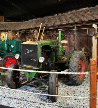 Es werden drei verschiedene Traktoren gezeigt. Rechts ein grüner Traktor der Firma Güldner. Links ein Hanomag und in der Mitte ein grüner Hürlimann. | © Auto Traktor Museum Bodensee
