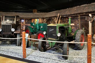 Es werden drei verschiedene Traktoren gezeigt. Rechts ein grüner Traktor der Firma Güldner. Links ein Hanomag und in der Mitte ein grüner Hürlimann. | © Auto Traktor Museum Bodensee