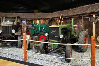 Es werden drei verschiedene Traktoren gezeigt. Rechts ein grüner Traktor der Firma Güldner. Links ein Hanomag und in der Mitte ein grüner Hürlimann. | © Auto Traktor Museum Bodensee