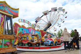 Auf dem Bild ist ein bunter Vergnügungspark mit einem Kinderkarussell, und einem Riesenrad im Hintergrund zu sehen. Mehrere Erwachsene und Kinder stehen davor oder gehen daran vorbei, während die farbenfrohen Fahrgeschäfte eine fröhliche Volksfestatmosphä | © Gemeinde Blaufelden