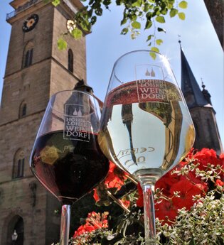 Zwei Gläser mit dem Logo Hohenloher Weindorf stehen auf einem Brunnen vor der Stiftskirche | © Touristikgemeinschaft Hohenlohe e. V. | Jürgen Koch