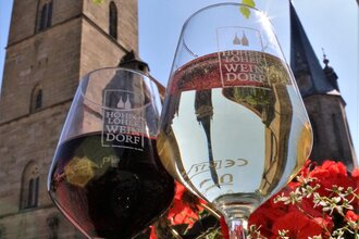 Zwei Gläser mit dem Logo Hohenloher Weindorf stehen auf einem Brunnen vor der Stiftskirche | © Touristikgemeinschaft Hohenlohe e. V. | Jürgen Koch