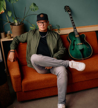 Person sitzt auf einem orangefarbenen Sofa neben einer grünen Gitarre. | © Jazzclub Schwäbisch Hall e.V.