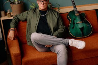 Person sitzt auf einem orangefarbenen Sofa neben einer grünen Gitarre. | © Jazzclub Schwäbisch Hall e.V.