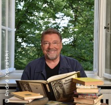 Ein Mann sitzt vor einem offenen Fenster mit Büchern auf dem Tisch. | © links im Bild