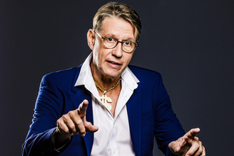 Ein Mann in einem blauen Anzug und weißem Hemd gestikuliert vor einem dunklen Hintergrund. | © Konzertkreis Triangel Compagnia Compostelli e.V.