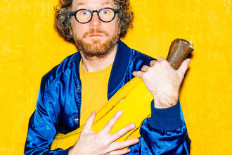 Ein Mann mit Brille und Bart hält ein großes gelbes Objekt vor einem gelben Hintergrund. | © Konzertkreis Triangel Compagnia Compostelli e.V.