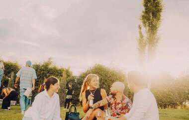 Leute sitzen auf einer Picknickdecke und trinken Wein etc.