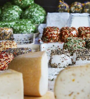 Verschiedene Käsesorten, im Vordergrund ist Hartkäse und im Mittel- und Hintergrund ist Frischkäse mit unterschiedlichen Gewürzen und Kräutern