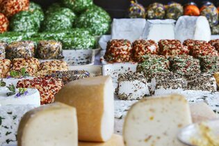 Verschiedene Käsesorten, im Vordergrund ist Hartkäse und im Mittel- und Hintergrund ist Frischkäse mit unterschiedlichen Gewürzen und Kräutern