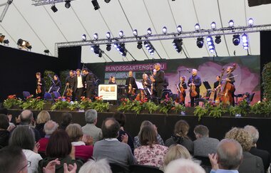 Auftritt Orchester auf einer der Bühnen. Im Vordergrund Publikum.