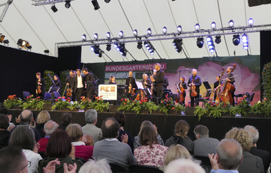 Auftritt Orchester auf einer der Bühnen. Im Vordergrund Publikum.