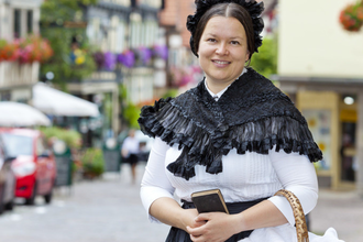 Frau in historischer Kleidung mit schwarzem Umhang und Haube in einer malerischen Altstadt. | © Stadt Besigheim