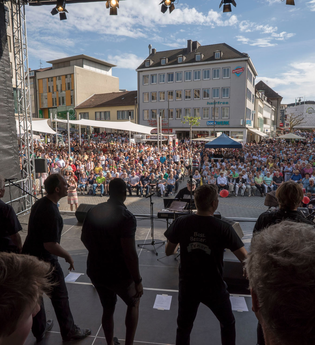 Blick von der Bühne auf den gut besuchten Kiliansplatz. Im Vordergrund ein Chor während des Auftritts.