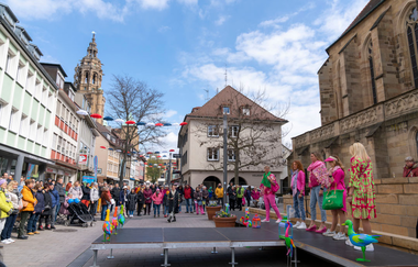 Modenschau in der Kirchbrunnenstraße. Mehrere Models sind auf dem Laufsteg. Im Hintergrund die gut besuchte Kirchbrunnenstraße und der Turm der Kilianskirche.