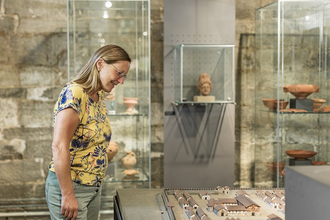 Eine Frau steht vor einer Vitrine mit römischen Funden | © Touristikgemeinschaft Hohenlohe e. V. | Barbara Wagner Fotografie