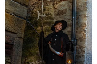Ein Nachtwächter in historischer Kleidung mit Laterne und Hellebarde steht vor einer Steinmauer. | © Stadt Besigheim