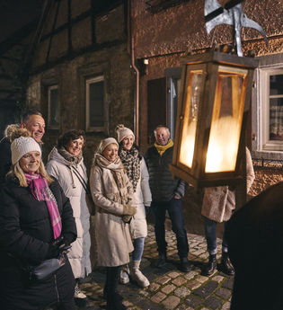Ein Gruppe Menschen hört gespannt einem Erzähler zu. Es ist Nacht und man schaut dem als Nachtwächter verkleideten Gästeführer über die Schulter. Er trägt eine Hellbarde und eine Laterne. | © Tourimia Tourismus GmbH