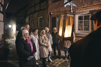 Ein Gruppe Menschen hört gespannt einem Erzähler zu. Es ist Nacht und man schaut dem als Nachtwächter verkleideten Gästeführer über die Schulter. Er trägt eine Hellbarde und eine Laterne. | © Tourimia Tourismus GmbH