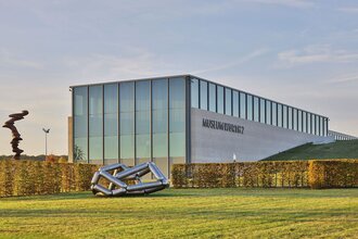 Das moderne Gebäude ist halb in die Erde gebaut, davor stehen zwei Skulpturen | © Touristikgemeinschaft Hohenlohe e. V. | Andi Schmid