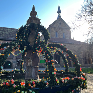 Geschmückter Osterbrunnen im Klosterhof im Hintergrund die Klosterkirche bei Sonnenschein | © Stadt Maulbronn