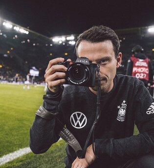 Fotograf Philipp Reinhard steht mit seiner Kamera am Fußballplatz im Stadion. | © philippreinhard.com_DFB