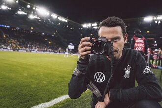 Fotograf Philipp Reinhard steht mit seiner Kamera am Fußballplatz im Stadion. | © philippreinhard.com_DFB