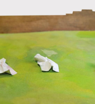 Drei zerknüllte weiße Zettel auf grünem Untergrund vor braunem Hintergrund.