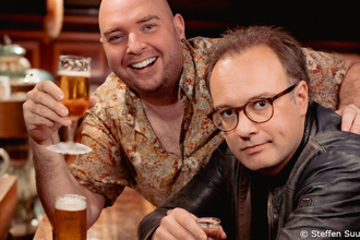 Zwei Männer in einer Bar, einer hält ein Bierglas, der andere trägt eine Brille und eine Lederjacke. | © Kultur- und Sportamt Stadt Bietigheim-Bissingen