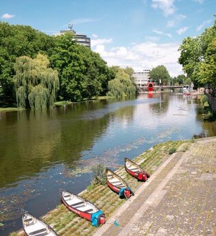 4 Kanus liegen auf der letzten breiten Stufe direkt am Neckar. In weiter Ferne ist das rote one man house erkennbar, auf der gegenüberliegenden Seite säumen hohe Bäume das Ufer