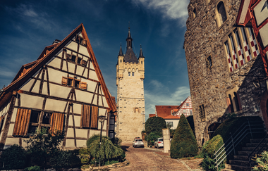 Blick in eine historische Gasse in der Altstadt Bad Wimpfen. Im Vordergrund ein Fachwerkhaus und ein Steingebäude, im Hintergrund ein historischer Burgturm aus Stein. | © Stadt Bad Wimpfen
