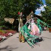 Zwei Personen auf Stelzen in fantasievollen Kostümen in einem blühenden Garten. | © Erlebnispark Tripsdrill