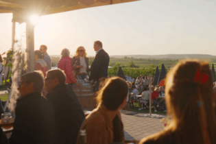 Mehrere Menschen sind in einer Hütte auf einem Weingut zu sehen. Die Sonne scheint | © Moser Burgfeld