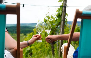 Zwei Liegestühle in den Weinbergen mit zwei Personen, die sich mit Weingläsern zu prosten | © Weingäe Stromberg-Zabergäu