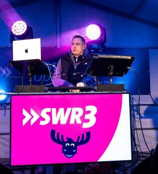 DJ auf Bühne mit Scheinwerfern an Pult mit SWR3 Logo in Pink