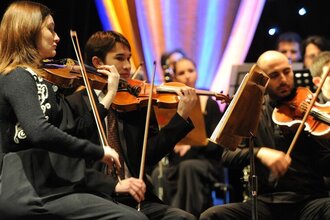 Ein Orchester spielt auf einer Bühne, mehrere Musiker mit Geigen. | © MCS