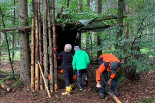 Drei Personen bauen eine Hütte aus Ästen und Zweigen im Wald. | © Forstamt Schwäbisch Hall