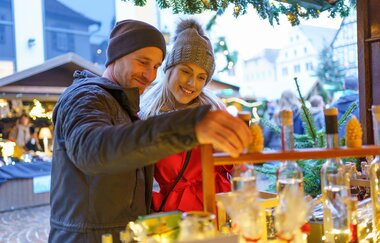 Ein Mann und eine Frau schauen sich einen Weihnachtsmarktstand mit Likören an. | © Stadt Bad Mergentheim