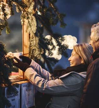 Ein Mann und eine Frau holen sich Tassen mit heißen Getränken bei einem Weihnachtsmarktstand.