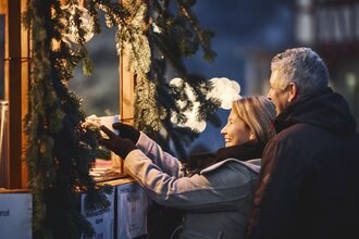Ein Mann und eine Frau holen sich Tassen mit heißen Getränken bei einem Weihnachtsmarktstand.
