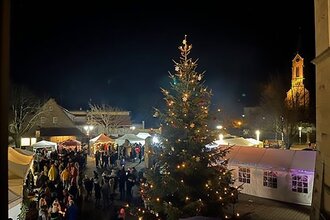 Weihnachtsbaum mit Verkaufsständen, im Hintergrund Kirchturm, Mühlbach