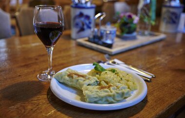 Ein Teller mit Maultaschen und Kartoffelsalat neben einem Glas Rotwein auf einem Holztisch in einer gemütlichen Besenwirtschaft | © Kraichgau-Stromberg Tourismus e.V.