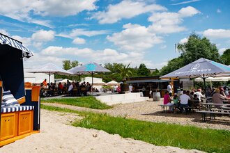Strandkorb auf Sandfläche, Personen sitzen an Kaffeehaustischen und Biertischen | © Heuchelberg Weingärtner eG