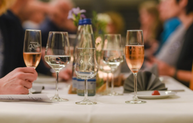 Im Fokus steht der Wein des Weingut Walz. Im Hintergrund sind verschwommen Gäste an einer Tafel zu erkennen.