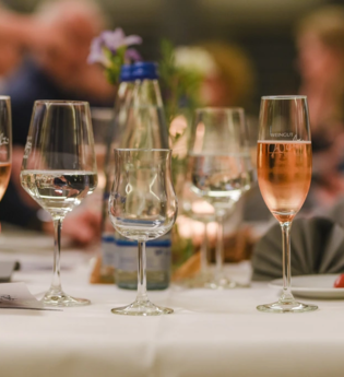 Im Fokus steht der Wein des Weingut Walz. Im Hintergrund sind verschwommen Gäste an einer Tafel zu erkennen.