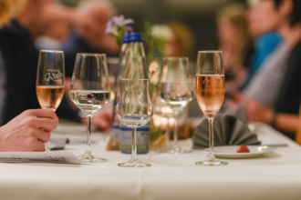 Im Fokus steht der Wein des Weingut Walz. Im Hintergrund sind verschwommen Gäste an einer Tafel zu erkennen.