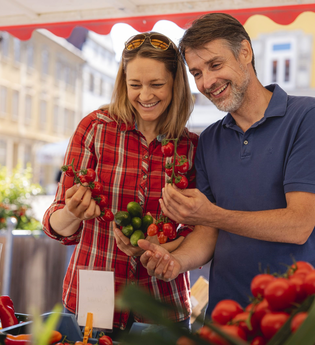 Eine Frau und ein Mann schauen sich Tomaten auf dem Wochenmarkt an | © PHILIPPREINHARD.COM