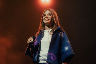 Die Künstlerin Zah1de steht auf der Bühne und hält ein Mikrofon in der Hand. Im Hintergrund leuchtet ein Scheinwerfer. | © William Krause